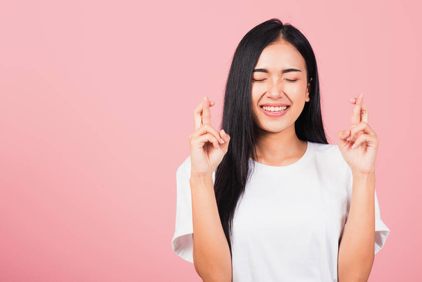 Asian happy portrait beautiful cute young woman smile have superstition her holding fingers crossed for good luck gesture studio shot isolated on pink background, Thai female with copy space - Foto, Imagen