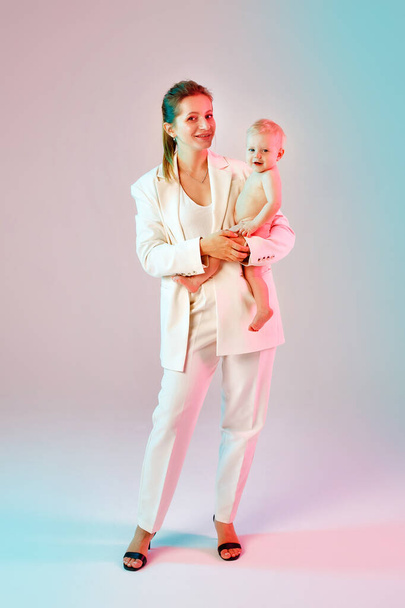 beautiful businesswoman holding little baby on hands, on grey - Foto, Bild