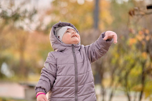 Una bambina con una giacca di dinosauro sta giocando con le foglie autunnali - Foto, immagini