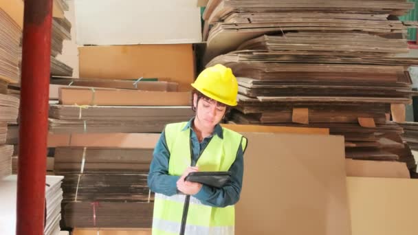Female worker in safety uniform and hard hat, supervisor inspector with a tablet, packaging stock order supply at factory warehouse, piles of stacking paper manufacture, recycling production industry. - Footage, Video