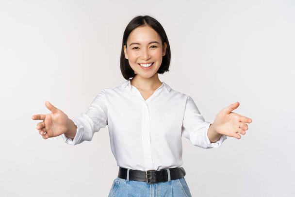 Bild einer lächelnden asiatischen Frau, die Gäste begrüßt, Geschäftsfrau, die offene Hände ausstreckt, grüßt, vor weißem Hintergrund steht. - Foto, Bild