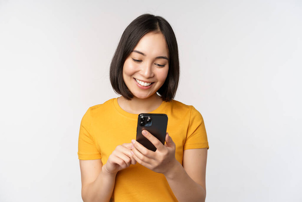 人々と技術の概念。スマートフォンでアジアの女の子を笑顔,携帯電話でテキストメッセージ,白い背景に立って. - 写真・画像
