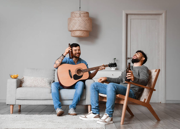 Male friends with bottles of beer and guitar at home - 写真・画像