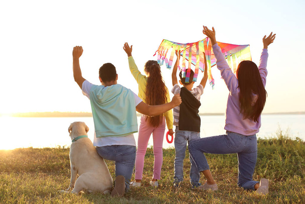 Ευτυχισμένη οικογένεια με χαρταετό και χαριτωμένο σκυλί κοντά στο ποτάμι - Φωτογραφία, εικόνα