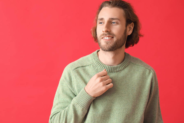 Красивый молодой человек в трикотажном свитере на цветном фоне - Фото, изображение