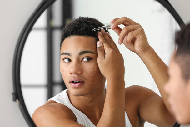 Афроамериканець, який використовує сироватку для росту волосся у ванній кімнаті. - Фото, зображення