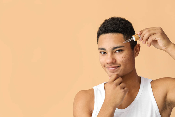 Fiatal afro-amerikai srác szérum bőrápoló színes háttér - Fotó, kép