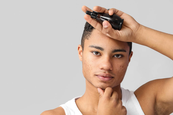 Молодой афроамериканец с сывороткой для ухода за кожей на сером фоне - Фото, изображение
