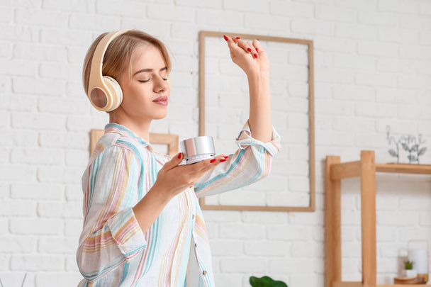 Woman with headphones and modern wireless portable speaker dancing in light room - Foto, Imagem