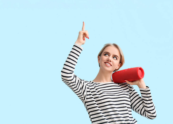 Woman holding modern wireless portable speaker and pointing at something on blue background - Photo, Image