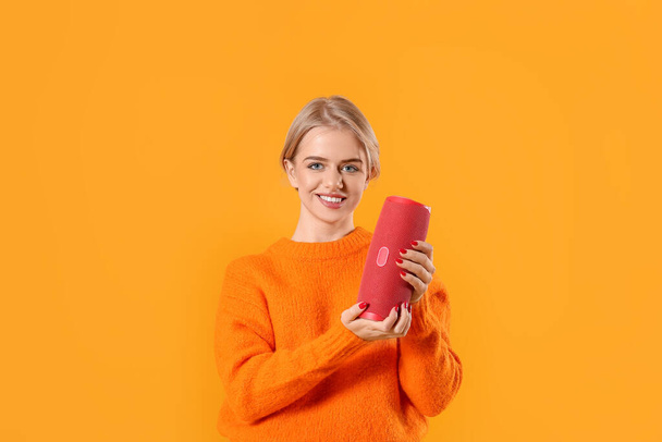 Young smiling woman with modern wireless portable speaker on color background - Foto, Imagen