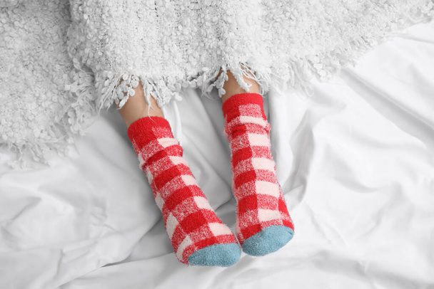 Vrouwelijke benen in gebreide sokken bedekt met ruitjes op bed. Begrip verwarmingsseizoen - Foto, afbeelding