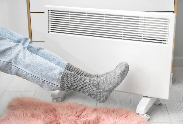 Žena v teplých ponožkách u radiátoru doma. Koncept otopné sezóny - Fotografie, Obrázek
