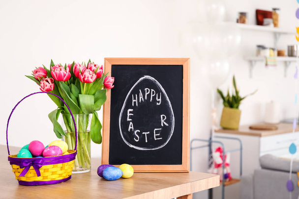 Kreidetafel mit Text HAPPY OSTER, Eier und Tulpen auf dem Tisch in der Küche - Foto, Bild