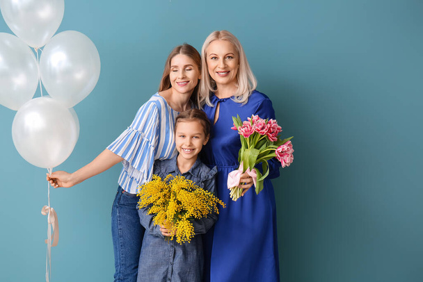 Νεαρή γυναίκα, η κορούλα της, μητέρα με λουλούδια και μπαλόνια σε μπλε φόντο - Φωτογραφία, εικόνα