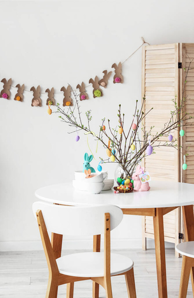 Louça e galhos de árvore decorados com ovos de Páscoa na mesa de jantar no interior do quarto - Foto, Imagem