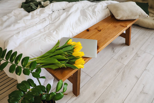Żółte tulipany i laptop na drewnianej ławce w sypialni - Zdjęcie, obraz