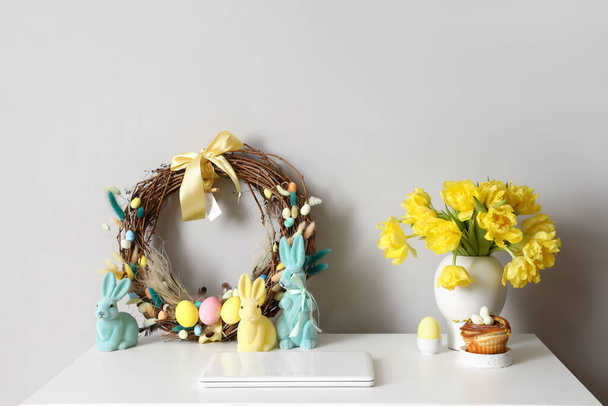 Lugar de trabajo con portátil, hermosos tulipanes y decoración de Pascua cerca de la pared de luz - Foto, Imagen