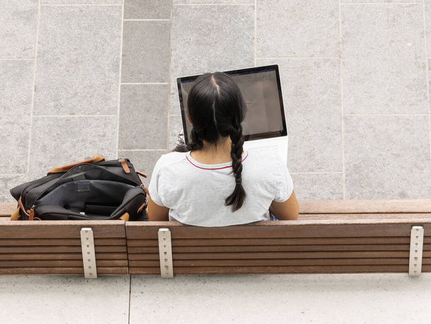 ベンチに座っている間、彼女の膝の上にラップトップコンピュータを保持している若い女性のトップビュー。本堂大学で学ぶ学生。ストリートビュー、選択フォーカス、ぼやけたテキストのためのコピースペース - 写真・画像