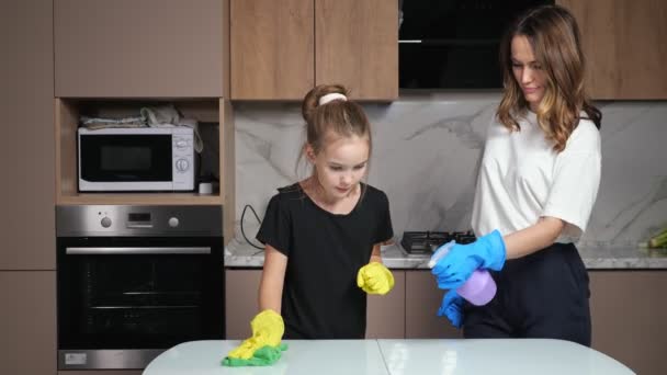 Madre e figlia adolescente con guanti colorati tavolo bianco pulito con spugna verde e detergente dando cinque in cucina a casa. - Filmati, video