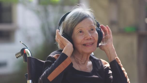 Ασιάτισσα ηλικιωμένη γυναίκα ακούει μουσική με ακουστικά στην πίσω αυλή. - Πλάνα, βίντεο
