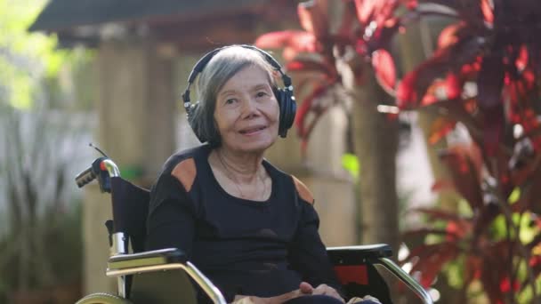 Ασιάτισσα ηλικιωμένη γυναίκα ακούει μουσική με ακουστικά στην πίσω αυλή. - Πλάνα, βίντεο