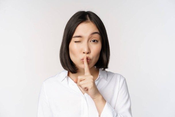 Close up portrait of young asian woman making hush, shhh shush sign, press finger to lips, dont speak, keep quiet gesture, white background. - Fotoğraf, Görsel