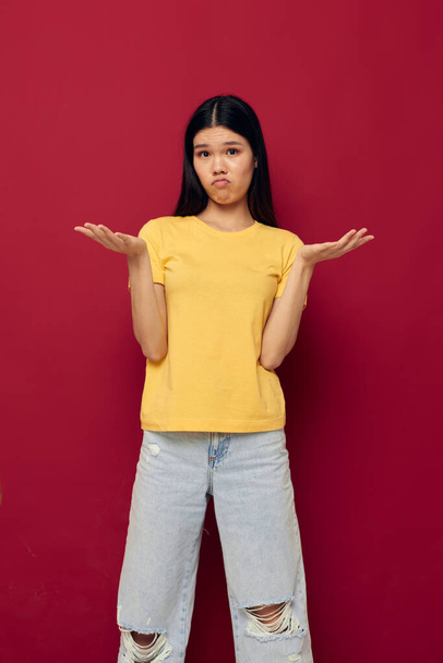 woman with Asian appearance gestures with his hands in a yellow t-shirt casual wear red background unaltered - Foto, afbeelding