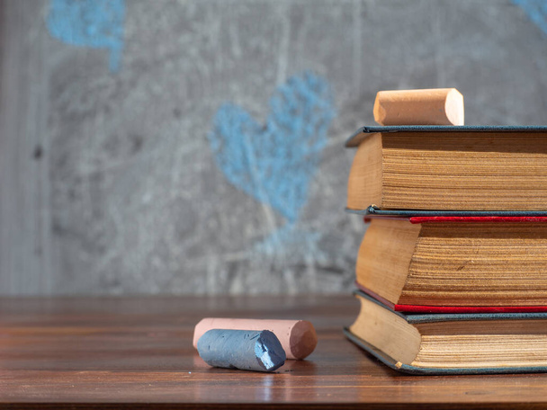 Livres et crayons d'école colorés sur une table en bois contre un tableau noir déconcentré avec des cœurs peints. Éducation et formation professionnelle, retour à l'école. - Photo, image