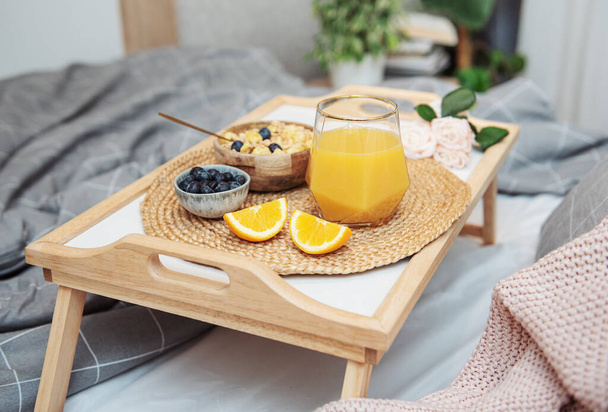 Gezond ontbijt. Sinaasappelsap, fruit en kom met granola op een dienblad. Ontbijt op bed.  - Foto, afbeelding