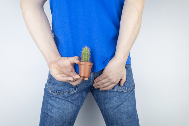 Concept. A man holds a cactus as a symbol of rectal pain. Varicose veins of the lower intestine. Pain in the rectum, hemorrhoids and pain in the excretory system of the body. Proctology - Zdjęcie, obraz