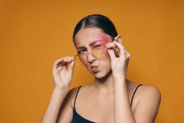 Portrait of beautiful young woman fashion glasses pink face makeup posing attractive look yellow background unaltered - Foto, Imagen