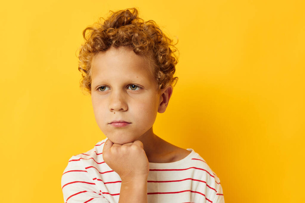 boy with curly hair in a striped t-shirt yellow background - Foto, Imagem