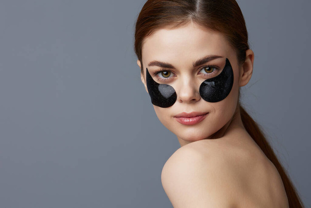 γυναίκα μπαλώματα ματιών στο πρόσωπο γυμνούς ώμους φροντίδα του δέρματος Γκρι φόντο. Υψηλής ποιότητας φωτογραφία - Φωτογραφία, εικόνα
