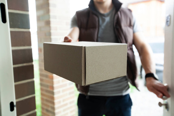 Deliveryman gives the carton box to the customer at the door of his house - Valokuva, kuva