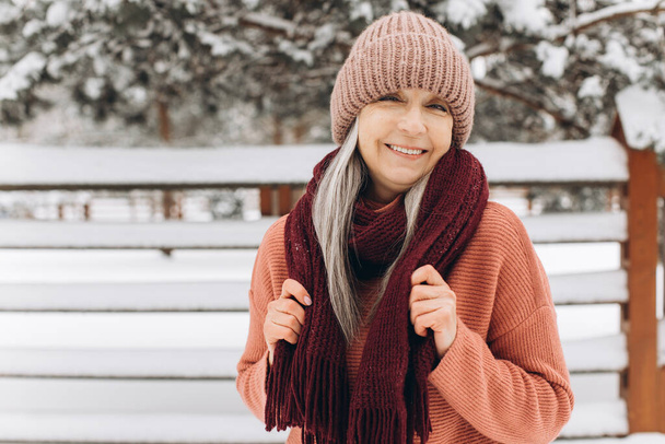 ニットのセーター、スカーフ、帽子を着た灰色の髪のシニア女性冬の背景. - 写真・画像
