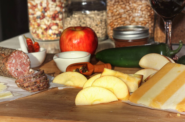 Salame di Peppercorn su vassoio con formaggio inglese e irlandese, mele affettate e spezie in cucina rustica con luce proveniente dalla finestra della cucina - Foto, immagini