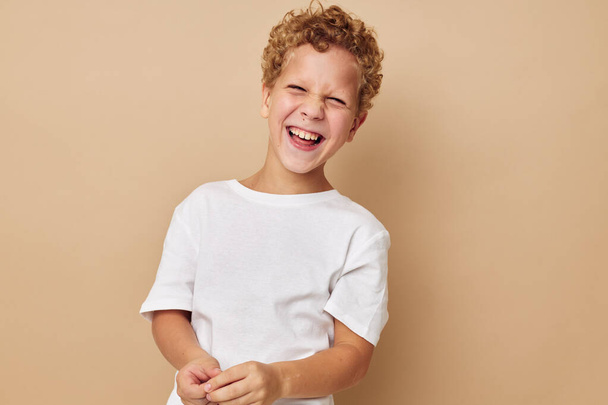 curly boy in a white t-shirt posing fun beige background - Fotó, kép