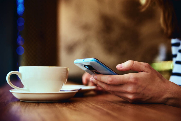Kobieta ręka używać smartfona w kawiarni, surfowanie w przeglądarce internetowej, mieć przerwę na kawę. Komunikacja internetowa i media społecznościowe - Zdjęcie, obraz