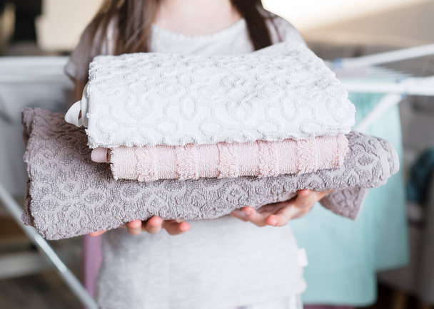 La chica sostiene una toalla doblada limpia en sus manos. Concepto de ayudar a los niños de la casa. Niña ayuda a su madre a doblar la ropa - Foto, Imagen
