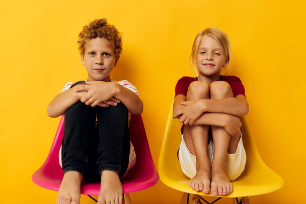 Small children childhood sitting on chairs together on colored background - Фото, изображение