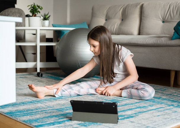 Girl trains online on a tablet for stretching with a fitball. Sports activities during the coronovirus pandemic. Quarantine. Study online - Fotoğraf, Görsel