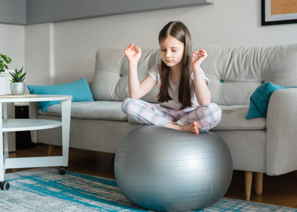 La ragazza si sta allenando con una palla da ginnastica a casa. Yoga per bambini. Sport durante la quarantena - Foto, immagini