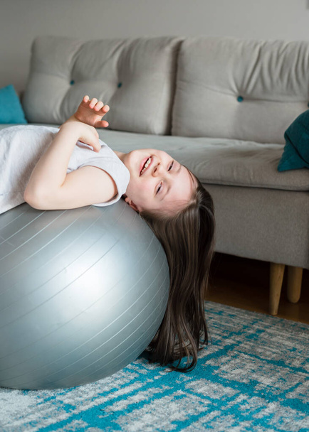 La chica está entrenando con una pelota de fitball en casa. Yoga infantil. Deportes durante la cuarentena - Foto, imagen