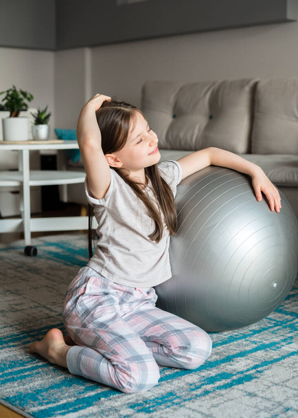 The girl is training with a fitball at home. Children's yoga. Sports during quarantine - 写真・画像