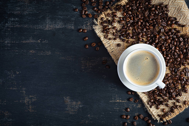 Cup of coffee with coffee beans on dark background. Mug of hot drink coffee - Photo, image