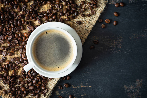 Cup of coffee with coffee beans on dark background. Mug of hot drink coffee - Foto, Imagem