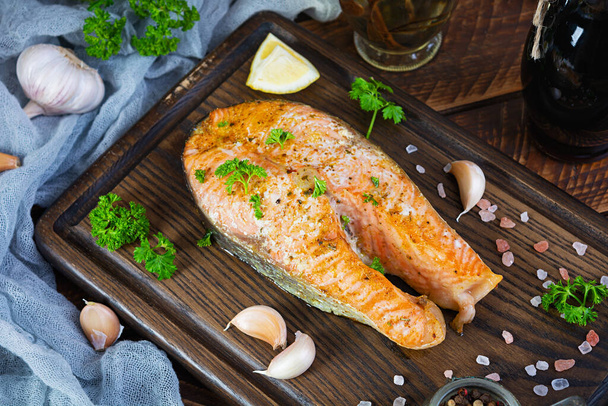 Baked salmon steak with herbs on wooden cutting board. Grilled salmon with salt and pepper - Zdjęcie, obraz