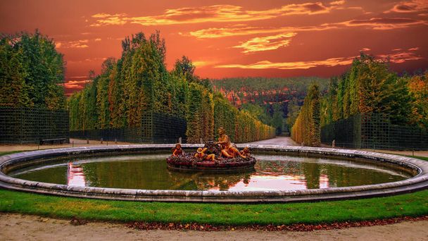 Neptun Fontána v zahradách slavného Versailles paláce proti krásné dramatické zatažené obloze při západu slunce. Versailleský palác byl královským zámkem a byl zařazen na seznam světového dědictví UNESCO - Fotografie, Obrázek