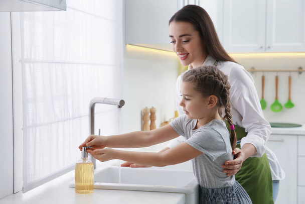 Mother and daughter washing hands with liquid soap in kitchen - Foto, afbeelding